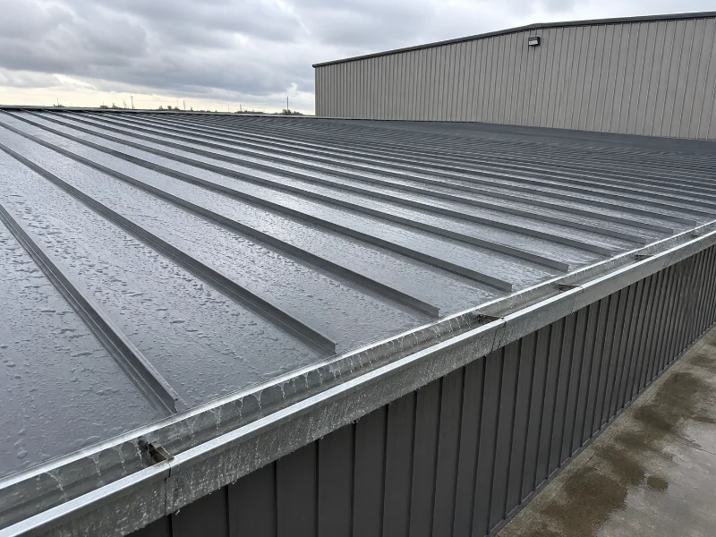 Low-slope standing seam metal roof on a steel building shedding rainwater toward the eave